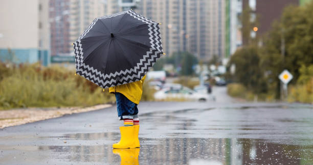 istock A small child in rainbow socks, yellow rubber boots and a jacket runs through puddles, has fun and plays after the rain. A picture of summer and autumn holidays. A child under an umbrella. 1414145486