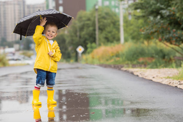 istock A small child in rainbow socks, yellow rubber boots and a jacket runs through puddles, has fun and plays after the rain. A picture of summer and autumn holidays. A child under an umbrella. 1414145491