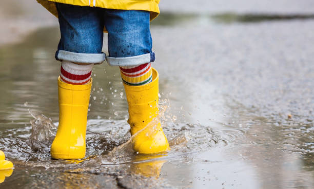 istock A small child in rainbow socks, yellow rubber boots and a jacket runs through puddles, has fun and plays after the rain. A picture of summer and autumn holidays. Legs close-up. 1414145606
