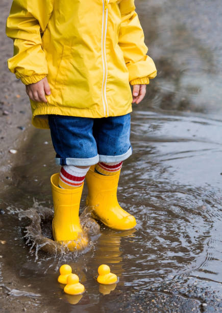 istock A small child in rainbow socks, yellow rubber boots and a jacket runs through puddles, has fun and plays after the rain. A picture of summer and autumn holidays. Legs close-up. 1414145607