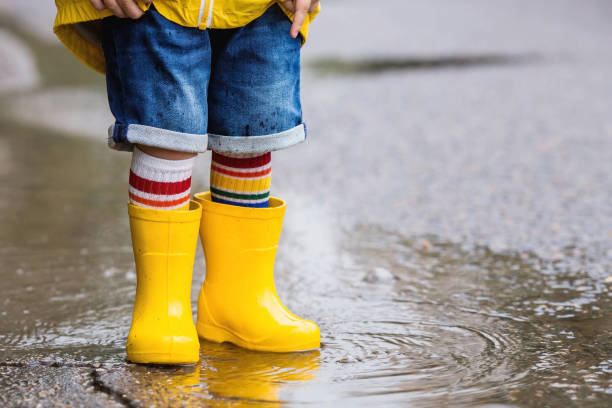 istock A small child in rainbow socks, yellow rubber boots and a jacket runs through puddles, has fun and plays after the rain. A picture of summer and autumn holidays. Legs close-up. 1414145610