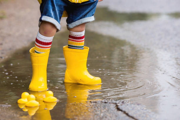 istock A small child in rainbow socks, yellow rubber boots and a jacket runs through puddles, has fun and plays after the rain. A picture of summer and autumn holidays. Legs close-up. 1414145612