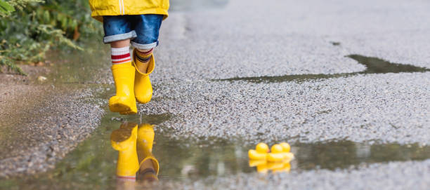 istock A small child in rainbow socks, yellow rubber boots and a jacket runs through puddles, has fun and plays after the rain. A picture of summer and autumn holidays. Legs close-up. 1414145616