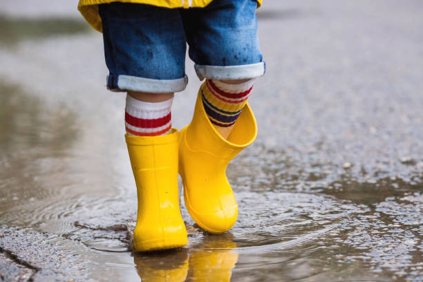 istock A small child in rainbow socks, yellow rubber boots and a jacket runs through puddles, has fun and plays after the rain. A picture of summer and autumn holidays. Legs close-up. 1414145617