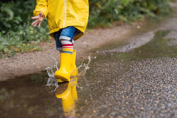 istock A small child in rainbow socks, yellow rubber boots and a jacket runs through puddles, has fun and plays after the rain. A picture of summer and autumn holidays. Legs close-up. 1414145618