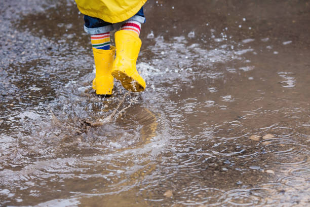 istock A small child in rainbow socks, yellow rubber boots and a jacket runs through puddles, has fun and plays after the rain. A picture of summer and autumn holidays. Legs close-up. 1414145628