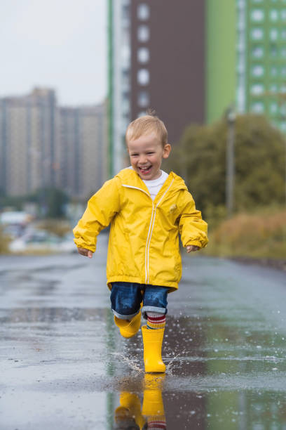 istock A small child in rainbow socks, yellow rubber boots and a jacket runs through puddles, has fun and plays after the rain. A picture of summer and autumn holidays. A happy child. 1414145787