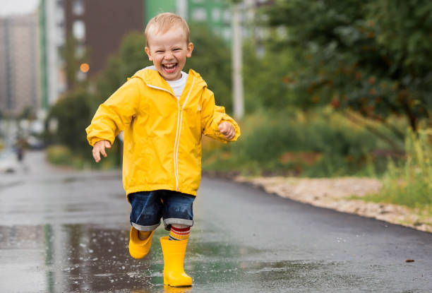 istock A small child in rainbow socks, yellow rubber boots and a jacket runs through puddles, has fun and plays after the rain. A picture of summer and autumn holidays. A happy child. 1414145798