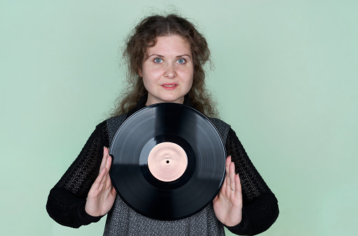 Young woman with curly hair listening to music using headphones holding vinyl disc