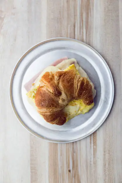 Croissant filled with ham and cheese on a silver-plated plate on a wooden table