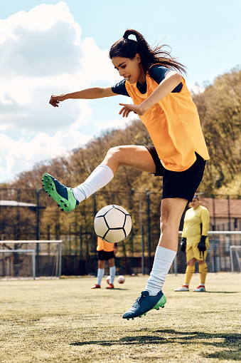 Female soccer player practicing with a ball during sports training on stadium.