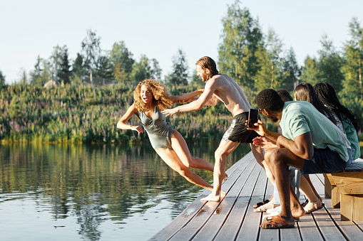 Full length shot of friends having fun at river with playful young man pushing girl in water