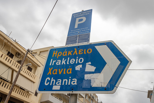 Directional Sign to Herakleion and Chania at Rethymnon Town on Crete, Greece. A parking sign behind has identifiable details.