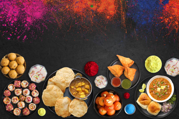 Assorted Indian Mahashivratri or Holi festival food like samosa, kachori, Kaju Katli, Puran Poli, dry fruits & Almond milk Thandai drink with Happy Holi wishes over black background with copy space. una variedad de mahashivratri indio o comida del festival holi como pav bhaji, dahi vada, gujiya, puri bhaji, gulab jamun, samosa, kachori, kaju katli, puran poli, frutas secas y leche de almendras bebida thandai con deseos happy holi sobre fondo negro con