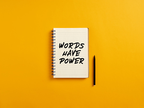 Notepad and black pen on yellow background with the message words have power.