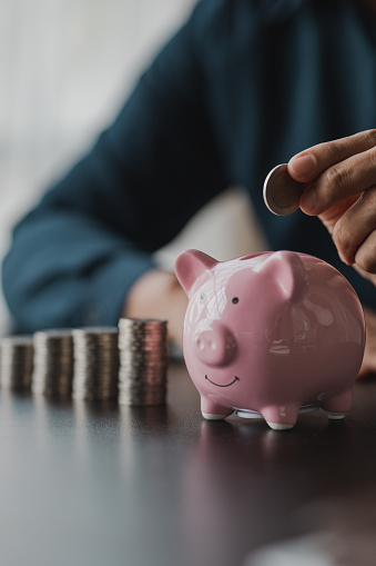 A businessman holding a coin in a piggy bank. Placing coins in a row from low to high is comparable to saving money to grow more. The concept of growing savings and saving by investing in stock funds.