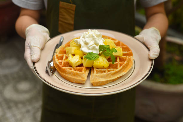 mani in guanti di gomma che tengono cialde belghe con ananas e gelato su un piatto - human hand baked food pineapple foto e immagini stock