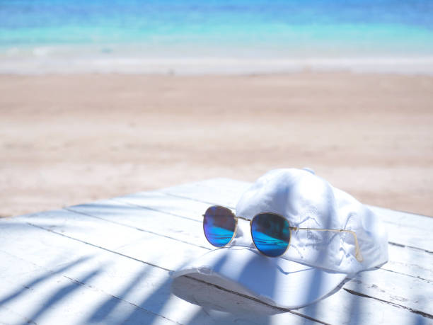 Close up blue sunglasses and hat on white table over summer beach background. Happy holiday concept.