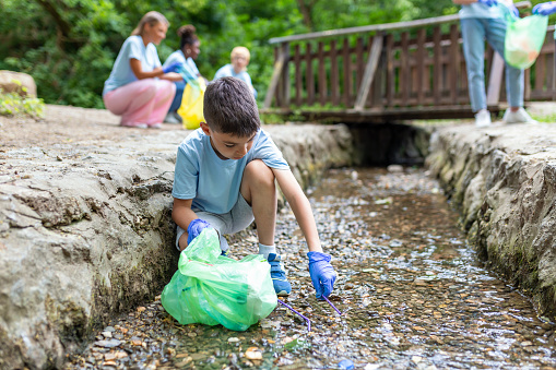 Kid boy handpicking gathering up garbage plastic straws garbage from the river at the park. World environment day.Environment concept.