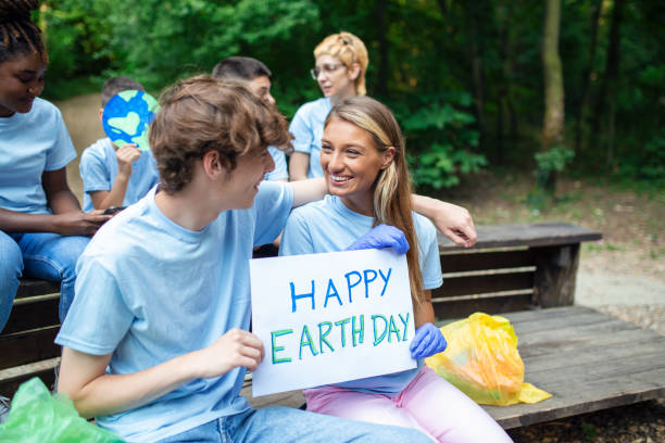 Female and male hands hold a piece of cardboard with the words Happy Earth Day. Happy and satisfied volunteers in nature clean and help maintain the environment.