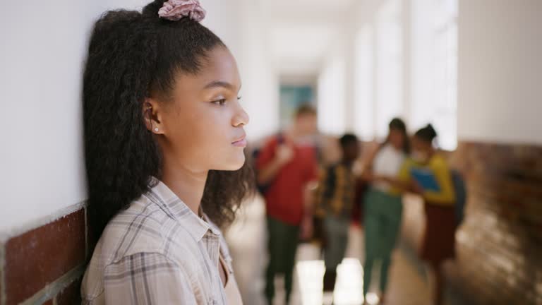 Bullied, anxious and depressed school girl nervous around students. Young child alone with no friends feeling lonely. Group pressure, feeling isolated, sad and unhappy at school