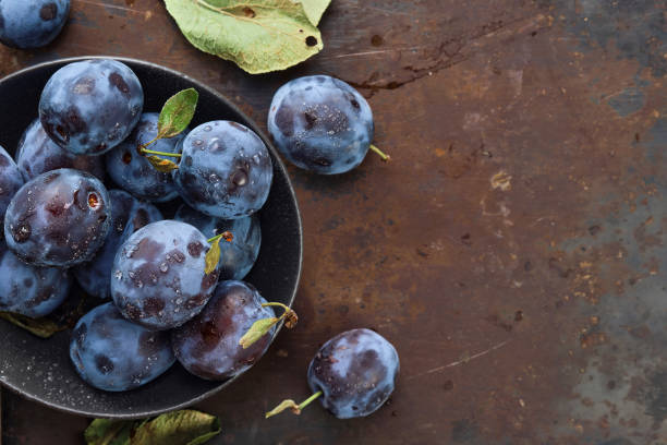 istock Fresh plums with leaves in a black plate on an old table, horizontal background, top view with copy space. Beautiful ripe prunes, harvesting fruits in autumn, eco products from the farm 1414174989