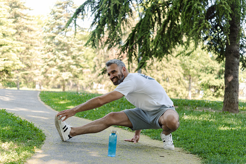 Portrait of a handsome mature man warming up for jogging in the park