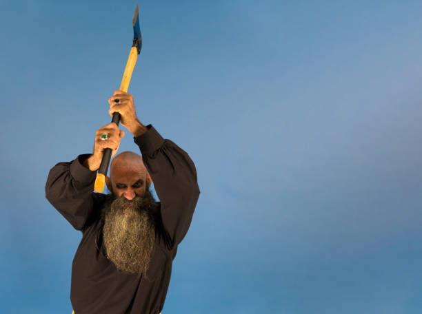 istock psycho lumberjack with long beard and shaved head who holds up an axe while has a wrath expression on his face and looking at camera 1414180714