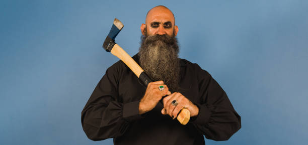 istock bald head man with long beard who holds an axe with both hands while looking at camera ahead a blue background 1414182462