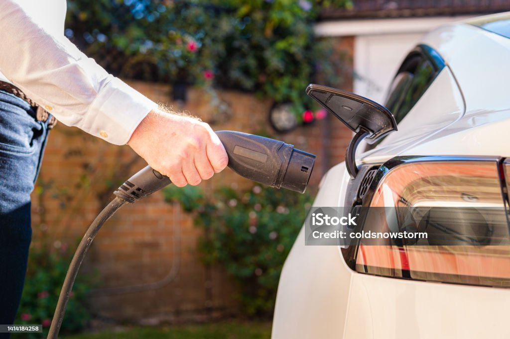 Man charging electric car at home Color image depicting a man charging his electric vehicle at home. Electric Vehicle Stock Photo