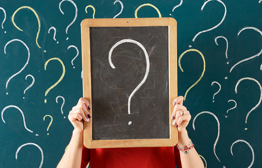 Woman holding small chalkboard with question mark in front of blackboard.