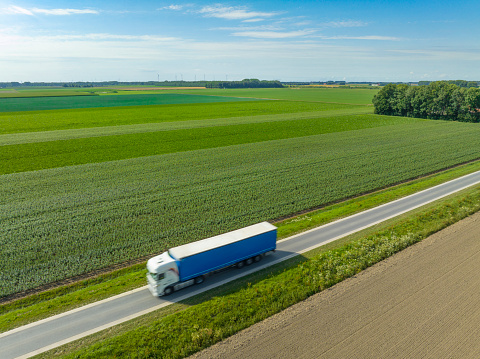 Truck hauling a trailer driving on a country road during a summer day in Flevoland, The Netherlands.