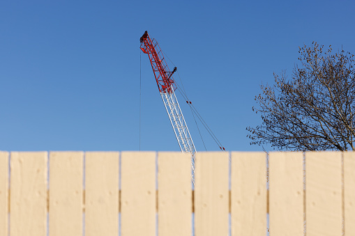 A large crane rises from behind an old wooden fence. Focus is on the crane.
