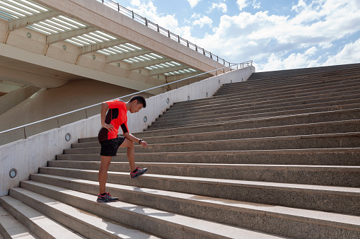 Hispanic sporty guy getting tired in front of stairs and blue sky with clouds