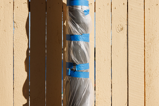 Plastic wrapped metal pole in front of an old wooden fence.