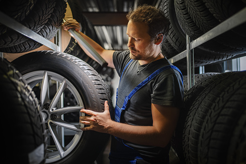 Hardworking experienced worker holding tire and he wants to change it In the tire store. Selective focus on tire.