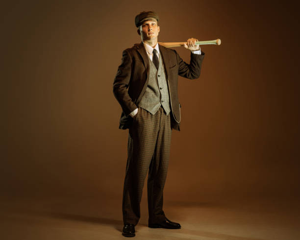 Retro style portrait of young man in image of english gangster, businessman wearing suit and cap standing isolated over dark vintage background. Retro style portrait of young man in image of english gangster, businessman wearing suit and cap standing isolated over dark vintage background. Concept of business, personality, emotions, fashion 1930s style men image created 1920s old fashioned stock pictures, royalty-free photos & images