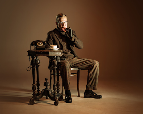 Retro style portrait of young man, writer and traveler wearing vintage style clothes isolated over dark brown background. Concept of business, personality, emotions, family, art, fashion