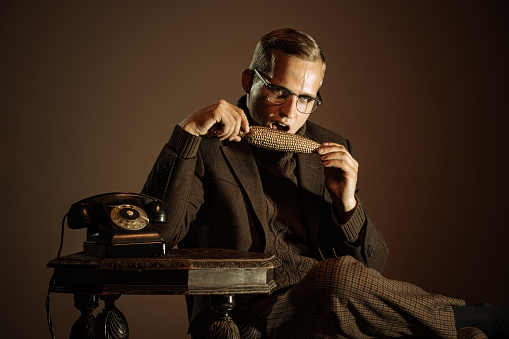 Gold. Retro style portrait of young man, writer and traveler wearing vintage style clothes isolated over dark brown background. Concept of business, personality, emotions, family, art, fashion