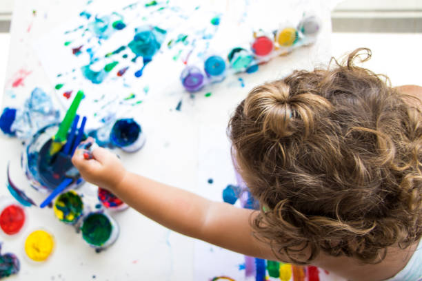little girl painting with brush and colorful paint on paper stock photo
