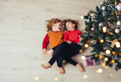 Happy funny children lying on the floor next to the Christmas tree. Christmas holiday. Real people, simple life. Copy space