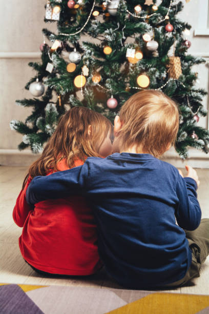 istock Brother and sister hugging and looking at the shining Christmas tree 1414207904