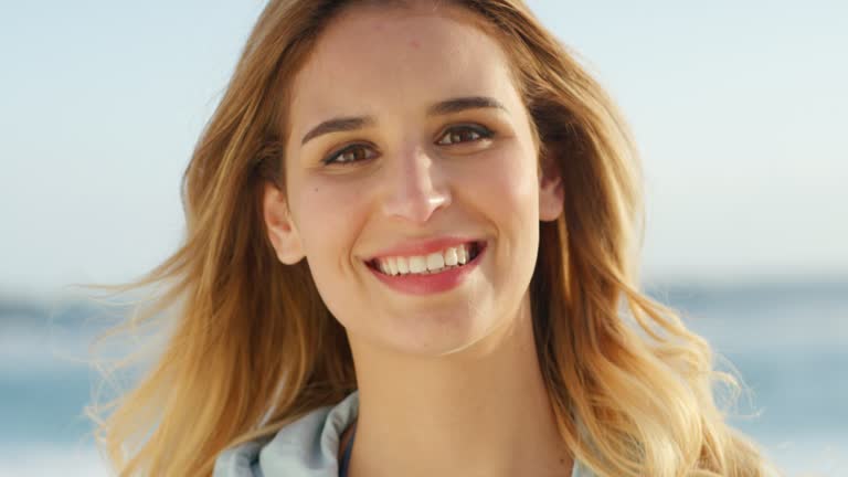 Happy, carefree and smiling woman having fun, relaxing by the beach in summer. Closeup portrait of the face of a young, joyful and beautiful female laughing and looking relaxed at the sea and seaside