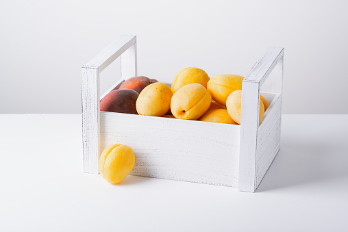 Wooden box with apricots and peaches isolated on white background.