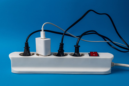 Multi-plug power strip with many connected devices on blue background. Concept of energy abuse. Waste and squandering of electricity