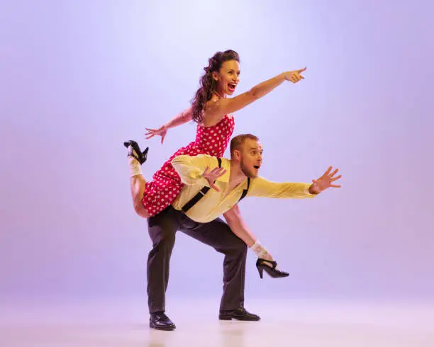 Photo of Emotional bright couple of dancers in colorful retro style attires dancing incendiary dances isolated on purple background in neon light.