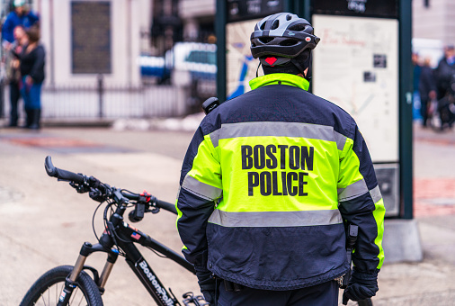 Boston, USA - Rear view of a police officer in the city's downtown district, with a Boston Police branded bicycle.