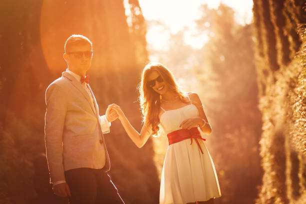 Stylish couple posing and dancing in sunset lights between trees