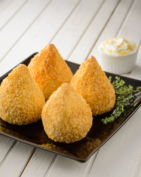 istock Four crispy delicious brazilian coxinhas or drumsticks on a black square plate with white wood table background 1414223094