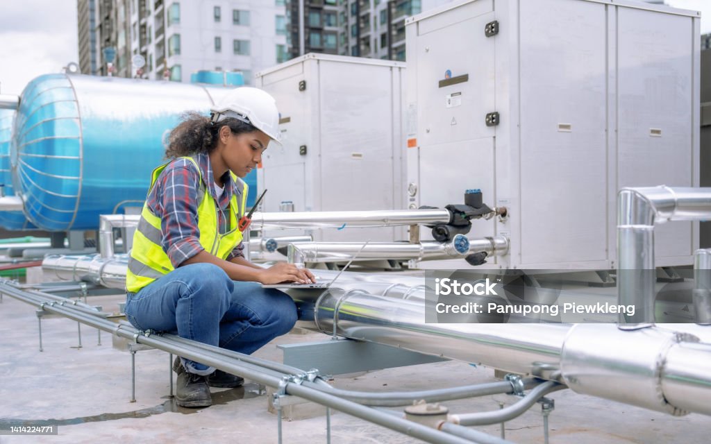 Female engineer inspects and controls the cooling system of a large factory air conditioner. Air Conditioner Stock Photo